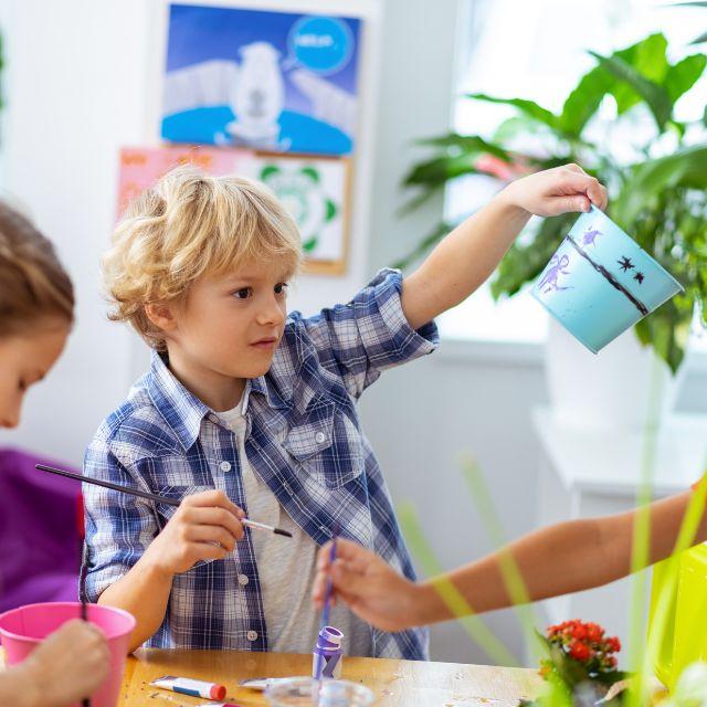 A child holding a paintbrush in one hand and a painted flowerpot in the other