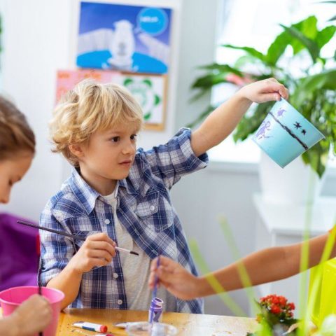 A child holding a paintbrush in one hand and a flowerpot in the other