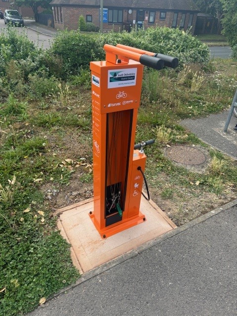 An orange bike repair station in the ground with a stand a pump